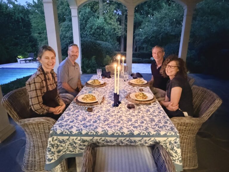 Four guests sharing dinner at a candlelit outdoor table at dusk