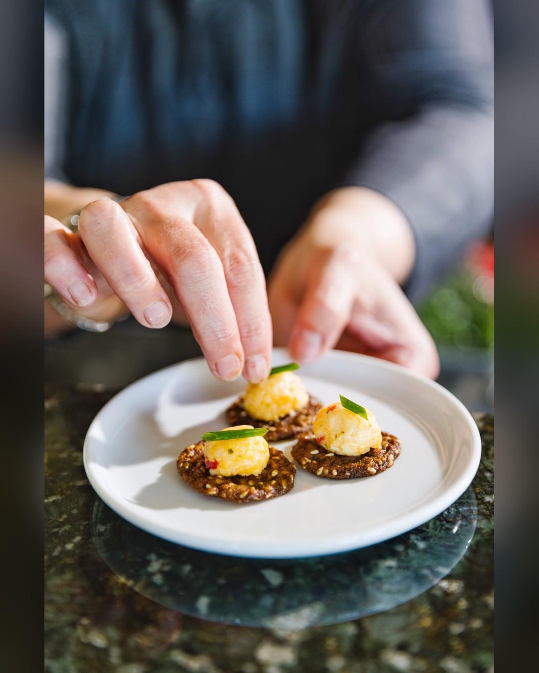 A chef's hands garnishing pimento cheese bites with chives