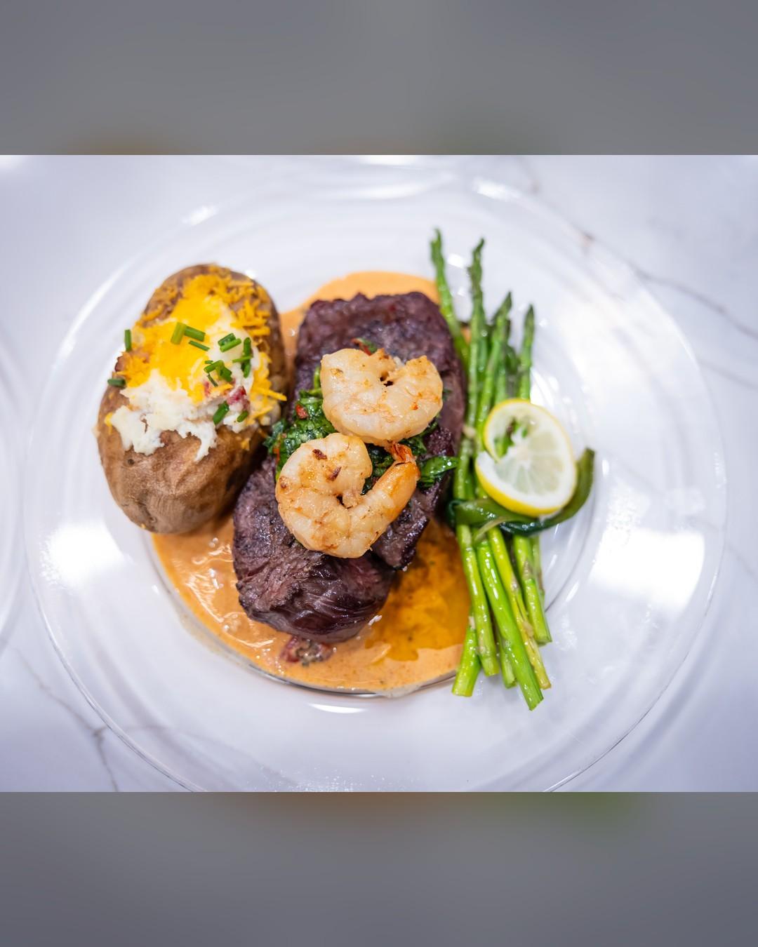 A plated steak with shrimp, baked potato and asparagus